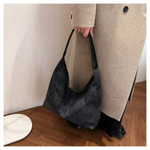 Detail of contrast stitching on dark grey matte hobo bag held by a model in a coat