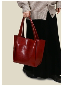 Detail of burgundy large faux leather tote bag with glossy finish on a grey cardigan model