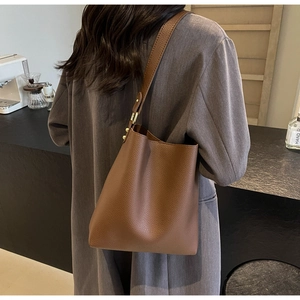 Detail of brown lychee grain leather bucket bag with gold metal buckle on model