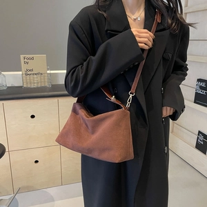 Brown suede shoulder bag with gold clasp shown on model wearing a black winter coat