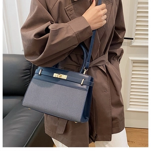 Detail of navy blue patchwork handbag with gold clasp worn by a model in a cozy room