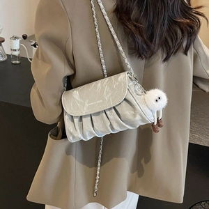 Sac bandoulière plissé gris avec chaîne argentée et pompon en peluche porté par un modèle