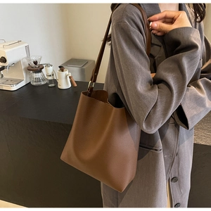 Close-up of brown pebbled leather bucket bag styled with a grey blazer in a cafe