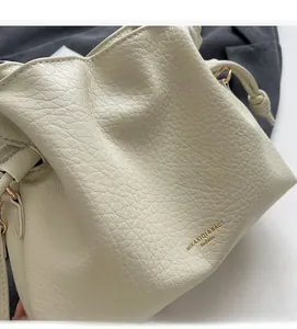 Détail du sac seau en cuir crème avec logo doré et texture grainée naturelle