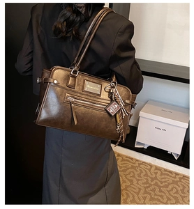 Detailed close-up of dark brown oil wax leather shoulder bag with creative bible pendant