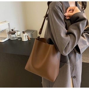 Detailed view of the brown lychee pattern leather bucket bag draped on a shoulder