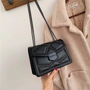 Detail of black quilted chain bag with bead studs hanging on a light pink wool coat
