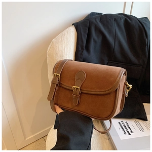 Detail of vintage brown frosted leather messenger bag with gold buckle on a white chair