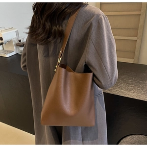 Detail of brown lychee grain leather tote bag with gold buckle worn in a cafe setting
