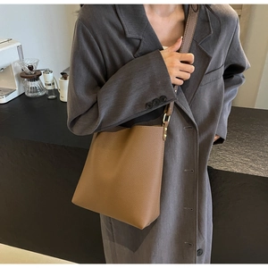 Close-up of brown lychee texture bucket bag on a model in a urban cafe setting