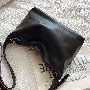 Minimalist black leather hobo shoulder bag with silver zipper on textured fabric background