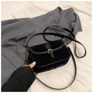 Detail of matte black crossbody bag with vintage gold buckle on textured fabric