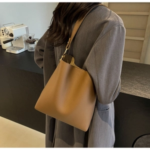 Brown lychee grain bucket bag with wide strap worn by a model in a modern cafe setting