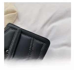 Close-up of black leather handbag featuring geometric rivets and precise stitching detail