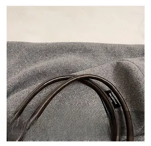 Macro shot of grey felt tote bag with brown leather handle and woven brand tag detail