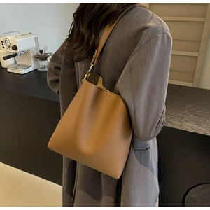 Brown lychee grain leather tote bag shown on shoulder in a modern lifestyle setting