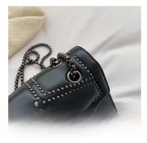 Detailed macro view of matte black leather bag with dark metallic rivets and chain strap