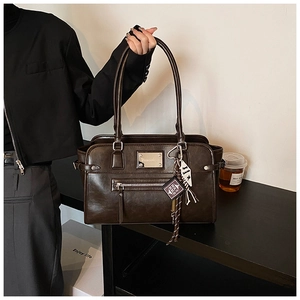 Detail shot of a dark brown glossy tote bag featuring a front zipper and stylish charms
