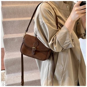 Close-up of vintage brown suede crossbody bag with flap and metal buckle on stairs