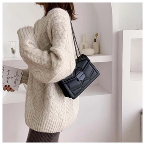 Detail of a black crossbody chain bag with stud accents worn over an oversized beige knit sweater