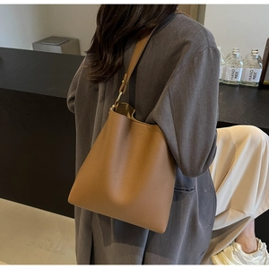 Close-up of camel brown tote bag with litchi texture on a model wearing a grey wool coat
