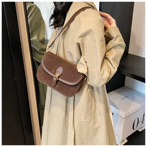 Brown suede shoulder bag with gold buckle shown on model in a modern room setting