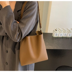 Brown lychee leather tote bag with minimalist hobo silhouette worn by a model