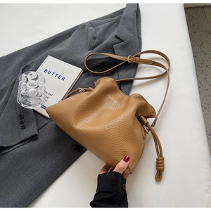 Détail du sac seau camel avec cordon et texture grainée sur une veste grise