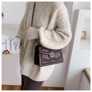 Detail of brown quilted crossbody bag with metal rivets and chain strap on knit sweater