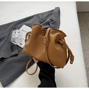 Détail du sac seau marron à cordon présentant une texture grainée et un logo élégant