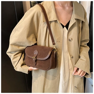Detail of dark brown matte suede crossbody bag with gold buckle on a beige trench coat