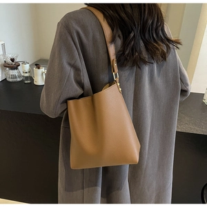 Close-up of brown litchi grain leather tote bag with gold buckle on shoulder strap