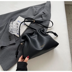 Détail du sac seau noir à cordon avec motif litchi et logo doré sur fond de veste blazer