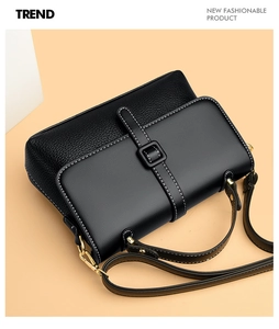 Detail of black leather messenger bag featuring white stitching and gold metal hardware