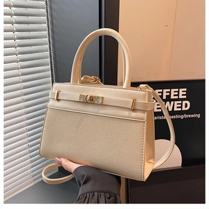 Detail of a creamy beige handbag with woven texture, leather handle and metal buckle