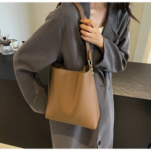 Brown lychee leather bucket bag with metal buckle shown on a model in a grey suit