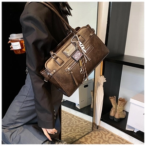 Detail of vintage matte brown tote bag with decorative book pendant and metal plaque