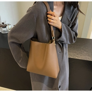 Brown lychee leather tote bag with adjustable strap worn on dark grey blazer