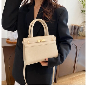 Detail view of cream-colored leather handbag with golden twist lock and twin handles