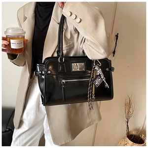Detail of glossy black patent leather tote bag with silver hardware and woven charm