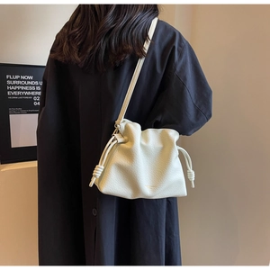 Gros plan du sac seau crème avec cordon de serrage en cuir grainé porté sur un manteau