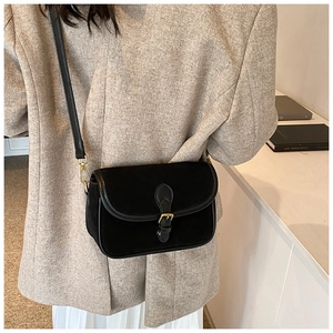 Close-up of matte black leather handbag with gold metal buckle on beige blazer