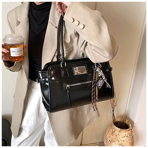 Detail of black glossy leather tote bag with silver logo plaque and decorative bag charms