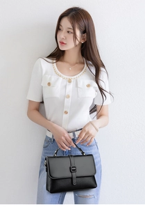 Detail of black satchel featuring smooth flap and pebble grain texture with metal buckle