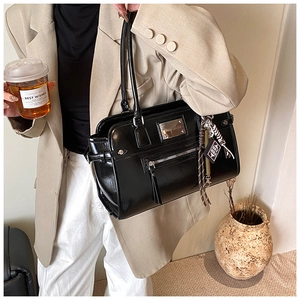 Model wearing a black glossy leather shoulder bag with tassels and silver metal logo plaque