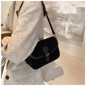 Detail of a vintage black suede crossbody bag with gold hardware worn with a plaid blazer
