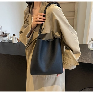 Detail of black pebble leather bucket bag shown on shoulder with minimalist styling