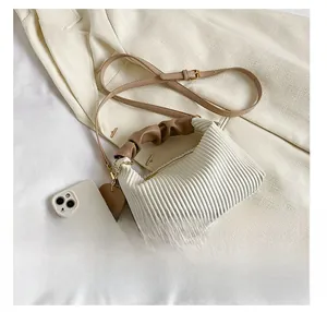 Close-up of pleated white handbag with brown scrunchie handle and heart tag detailing