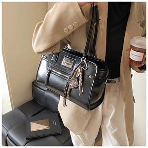 Detail of glossy black tote bag with silver heart charm and metal hardware accents