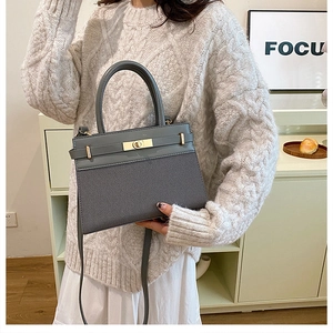 Detail of gray crossbody bag featuring mixed textures and elegant gold metal twist lock